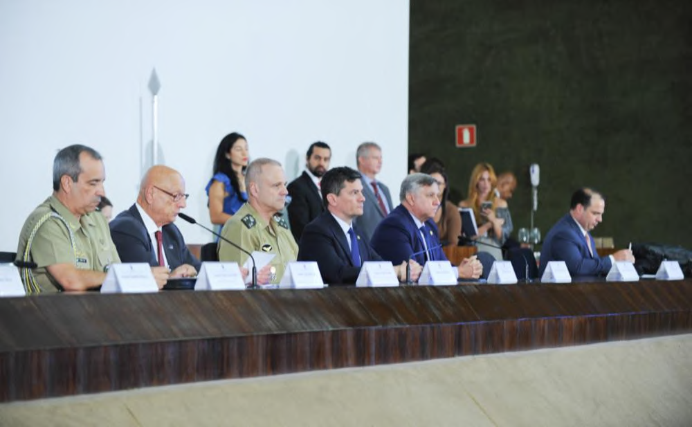 Participantes sentados à mesa de uma reunião parlamentar.