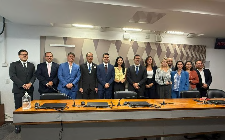 Grupo posando junto à mesa de uma sala de comissão.